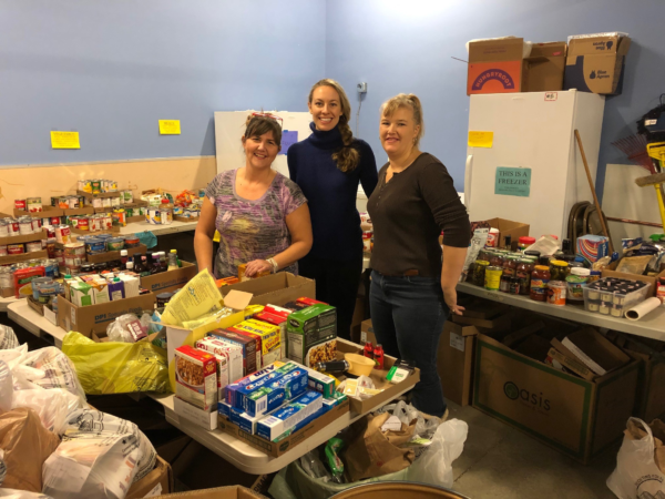 Three people standing in a storeroom filled with tinned food and boxed groceries