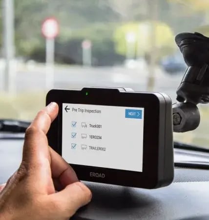 Hand ticking a Pre Trip Inspection checklist for a truck and trailer on a dash-mounted EROAD device