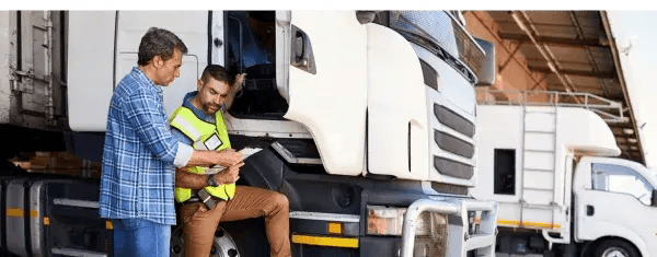 Two people checking a document beside a truck at a loading dock
