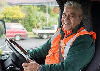 Smiling driver in a hi-vis vest behind the wheel of a truck