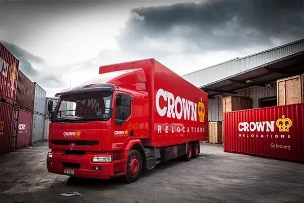 Red Crown Relocations truck parked beside shipping containers at a depot