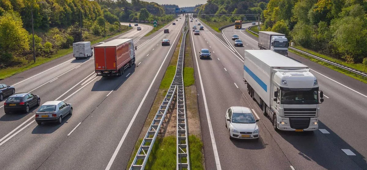 Trucks and cars travelling on a multi-lane divided highway lined with trees