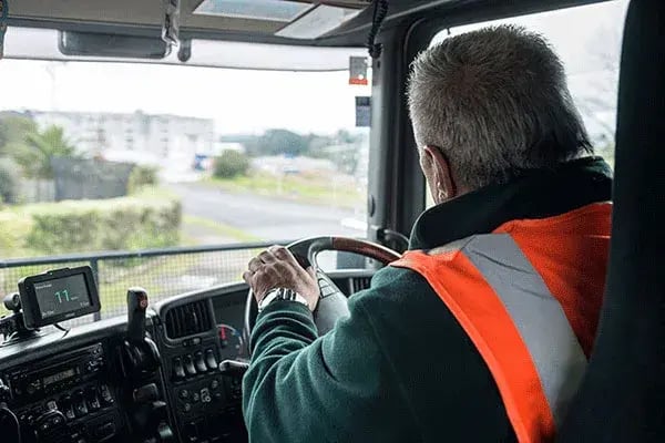 Truck driver in a hi-vis vest at the wheel, with an in-cab screen mounted on the dash