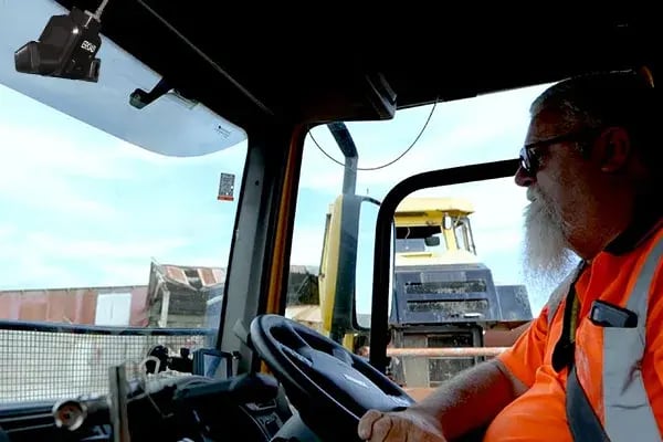 Driver in hi-vis at the wheel of a truck, with a dashcam mounted on the windscreen