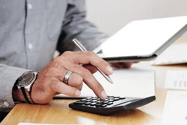 Person using a calculator and pen at a desk beside a tablet