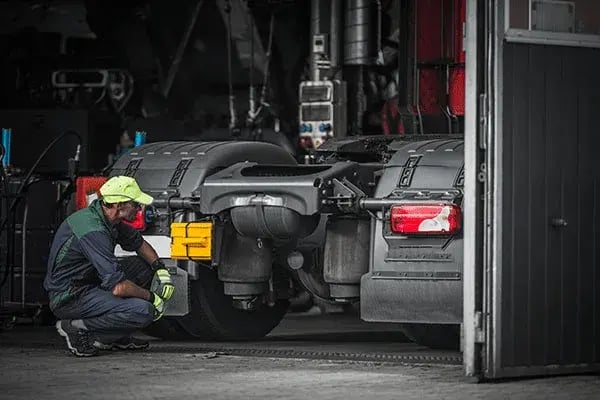 Mechanic crouching behind a truck in a workshop, inspecting its rear
