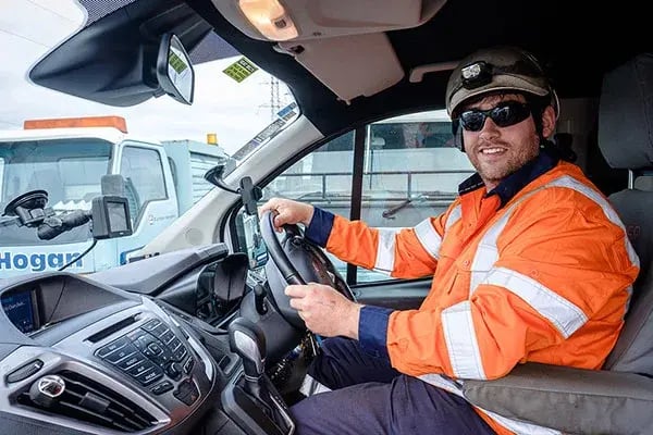 Smiling driver in hi-vis and a hard hat at the wheel of a work vehicle
