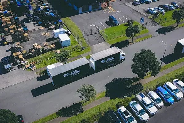 Aerial view of two box trucks on a road between an industrial yard and a car park