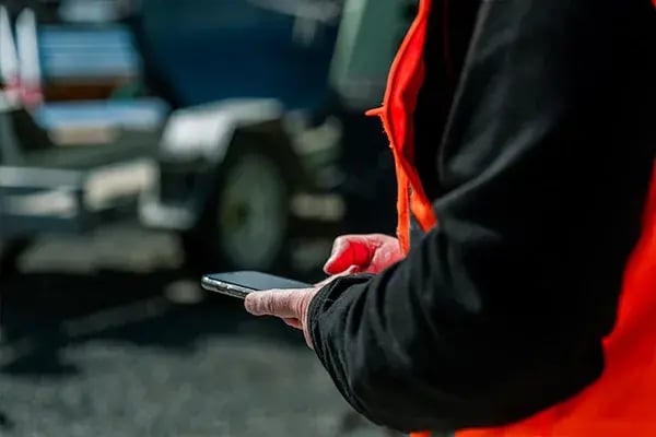Worker in a hi-vis vest holding a mobile phone near parked vehicles