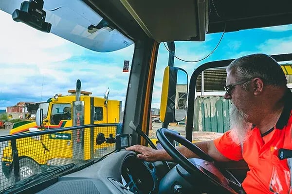 Truck driver in hi-vis at the wheel, with a dashcam mounted at the top of the windscreen