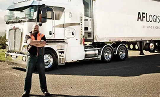 Driver in hi-vis standing in front of a white prime mover and trailer