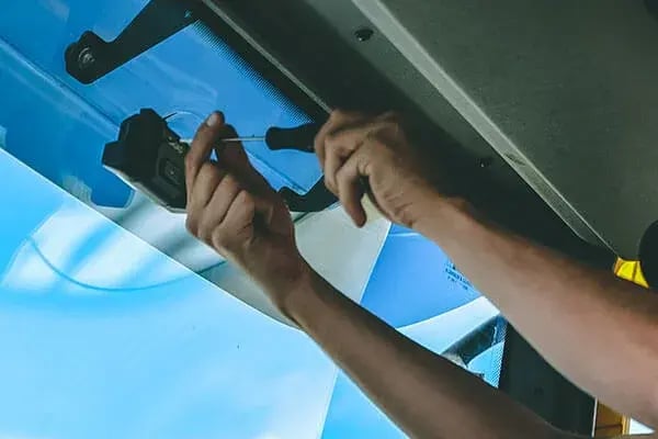 Hands fitting a dashcam to the top of a vehicle windscreen with a screwdriver