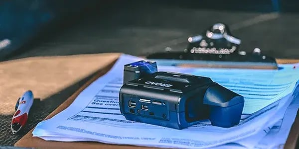 EROAD dashcam resting on a clipboard of paperwork beside a pen