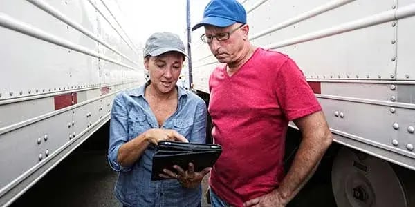 Two people in caps looking at a tablet together between two trailers