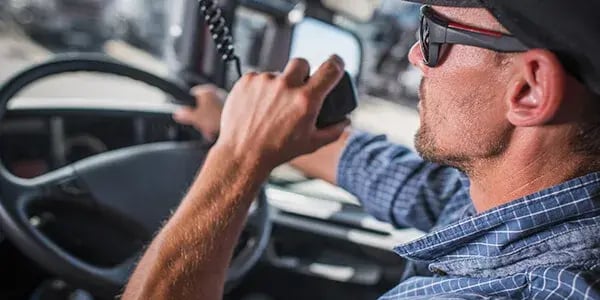Driver in sunglasses holding a radio handset at the wheel of a truck