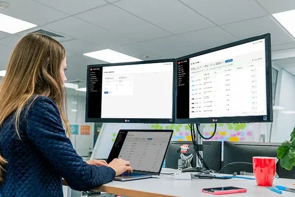 Person at a desk using a laptop and two monitors showing EROAD fleet software lists