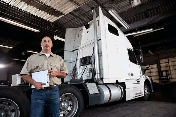 Person holding a clipboard in front of a white prime mover in a truck depot