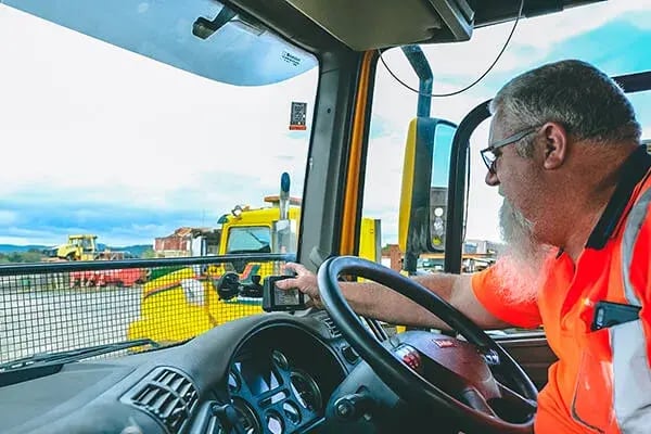 Truck driver in hi-vis reaching for a dash-mounted device inside the cab