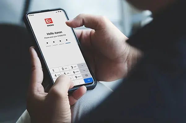 Hands holding a phone showing the EROAD Assist login screen asking for an Ehubo PIN
