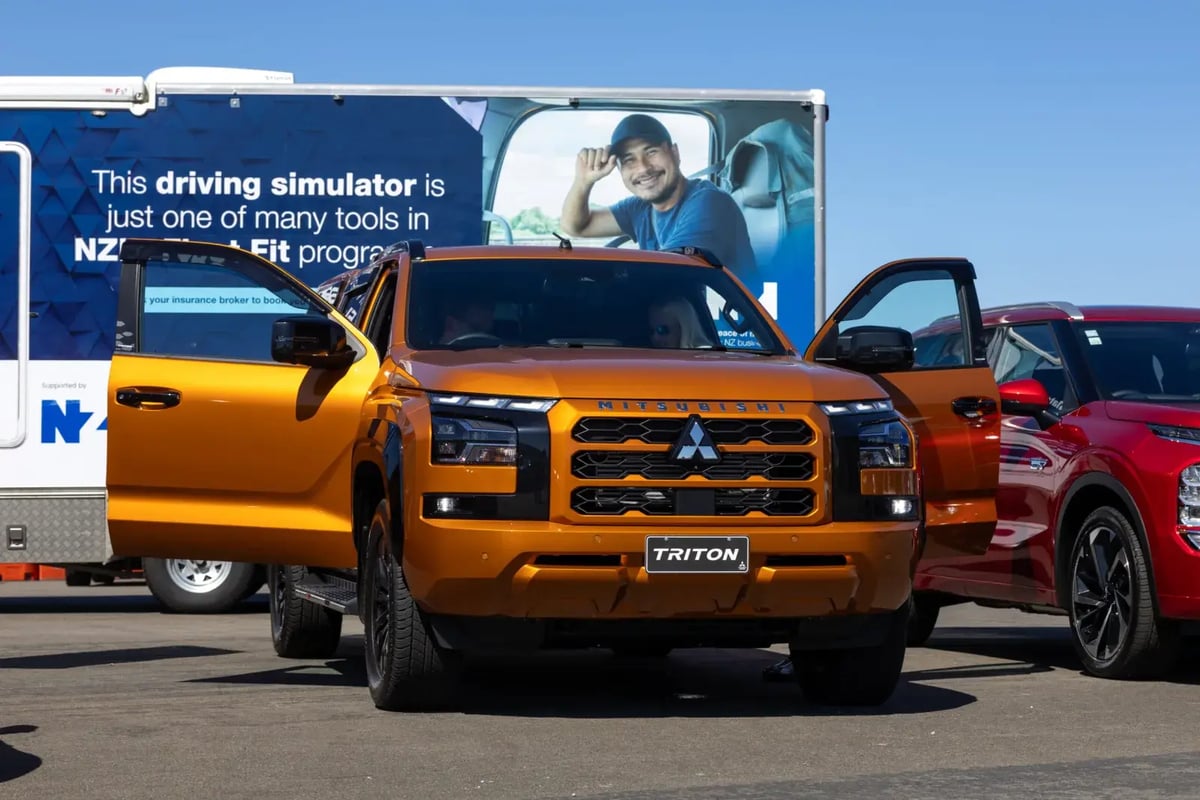 Orange Mitsubishi Triton ute with doors open in front of a driving simulator trailer at Fleet Day