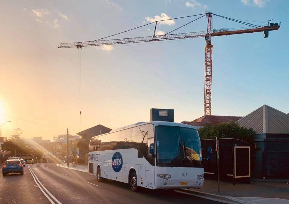 White coach on a suburban street in low sunlight with a tower crane behind