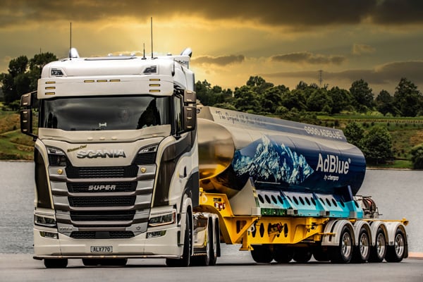 Scania truck hauling an AdBlue tanker trailer under a golden evening sky