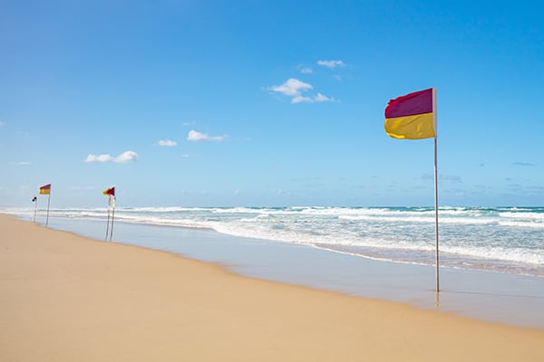 Red and yellow patrol flags on a sandy beach with surf rolling in