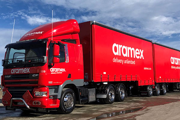 Red Aramex DAF truck and curtainsider trailers carrying the delivery unlimited slogan
