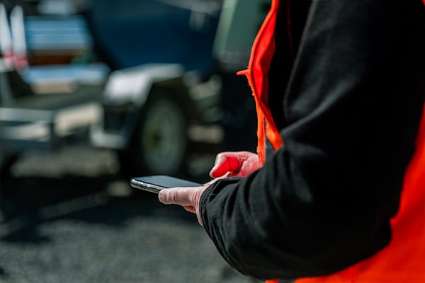 Worker in a hi-vis vest holding a smartphone beside parked vehicles