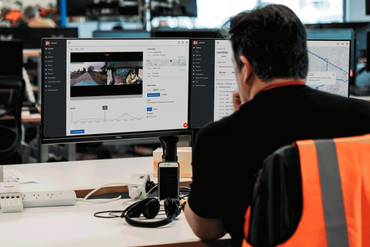 A fleet manager at a desk reviewing camera footage and trip history on two EROAD screens
