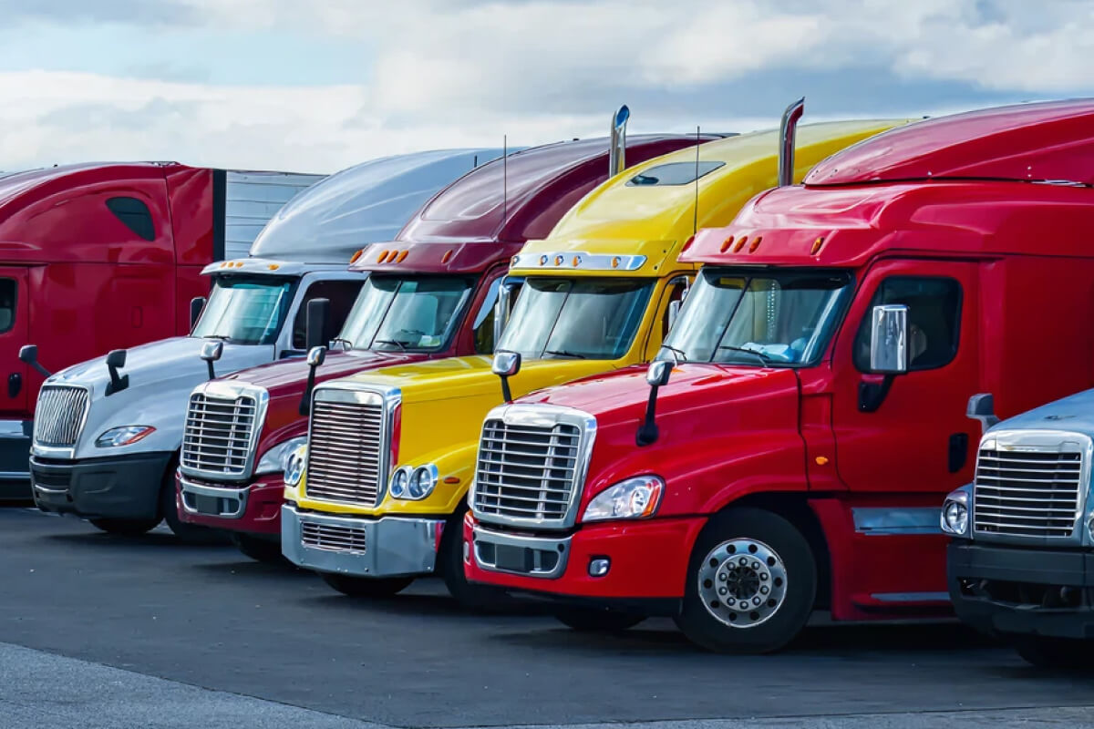 Row of red, yellow, maroon and silver semi trucks parked side by side