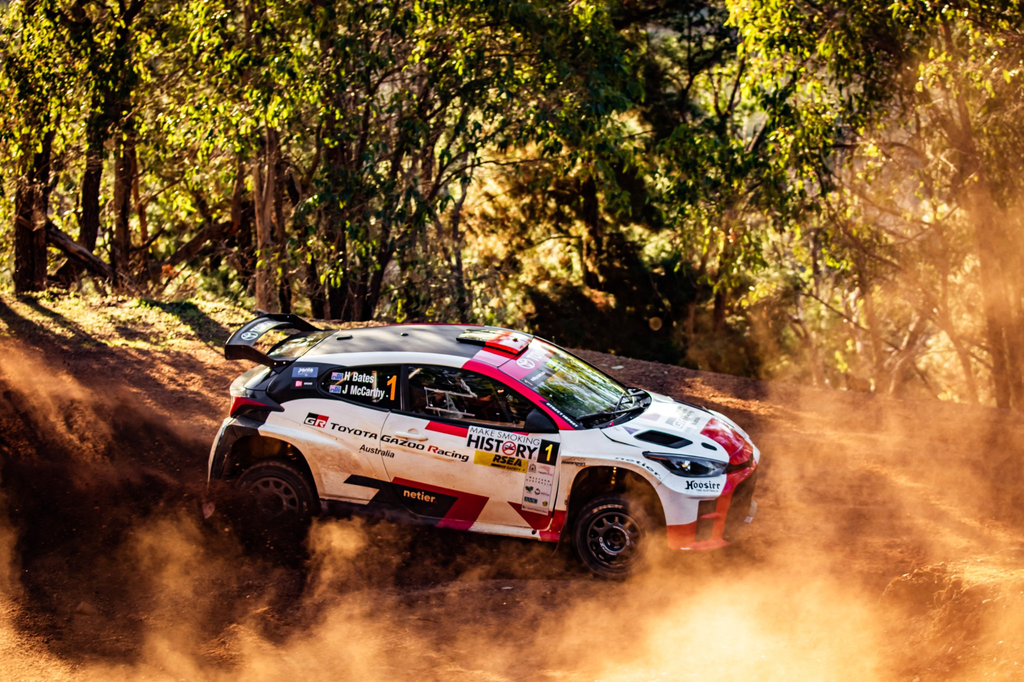 A rally car on a gravel stage in backlit dust