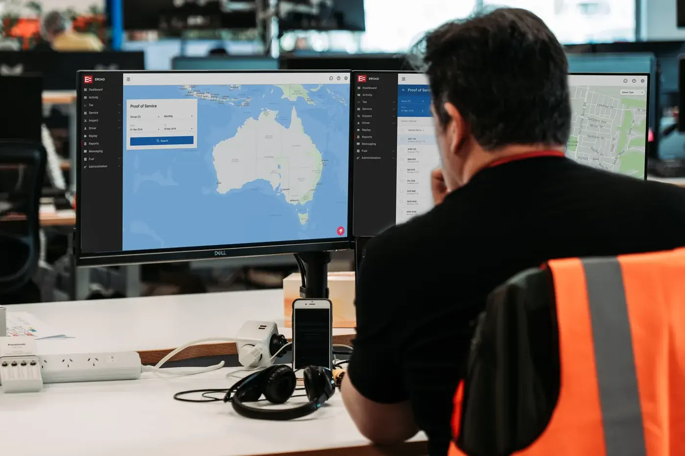 An operator in a hi-vis vest viewing the Proof of Service screens in MyEROAD across two monitors