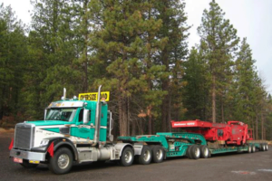 Redmond Heavy Hauling green and white truck hauling red equipment loader, oversize load