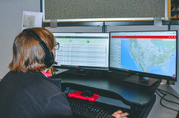 Dispatcher with two computer screens showing truck locations on map and load and driver hours available info in real time